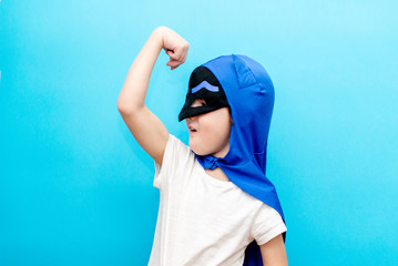 Cute little boy in a superhero costume on a colored background
