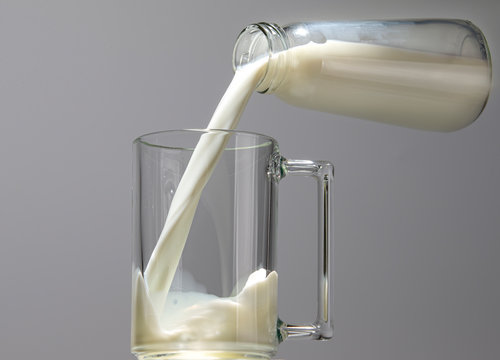 Milk Stream Pouring From A Bottle Into A Glass Mug