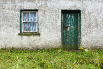 Run down Irish cottage with green door and window with chipped paint