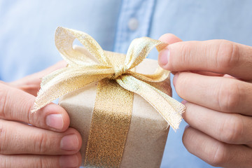 Man holding gift with gold ribbon, man's hands, closeup