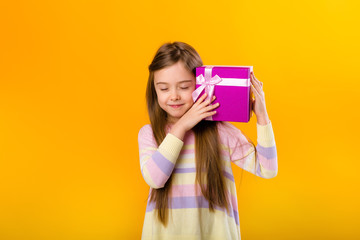 happy little girl with long hair holding a pink gift box on a yellow background isolate