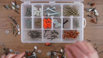 Timelapse of hand putting and organizing screws, nails, bolts and washers into a transparent plastic organizer box on a table - Powered by Adobe