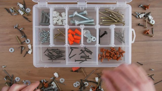 Timelapse of hand putting and organizing screws, nails, bolts and washers into a transparent plastic organizer box on a table