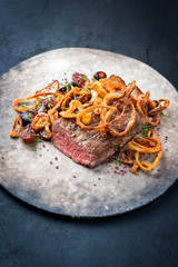 Traditional dry aged sliced roast beef with fried onion rings and potatoes served as closeup on a modern design plate