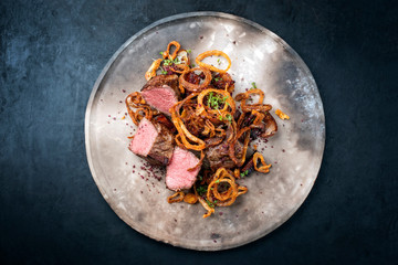 Traditional dry aged sliced beef tenderloin with fried onion rings and potatoes served as top view...