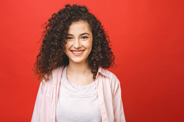 Happy cheerful young woman with curly hair rejoicing at positive news or birthday gift, Student girl relaxing after college isolated over red background.