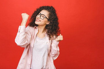 Photo of cheerful beautiful young woman standing isolated over red wall background. Looking camera showing winner gesture.