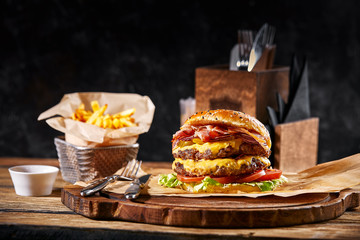 Fresh and juicy hamburger on a paper pillow with beer on a wooden table. Dark background,...