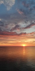 Amazingly vibrant landscape of an alarming dramatic sunset in orange tones. The setting sun is reflected in sea water. Light clouds are painted in different colors from blue to red in the sky