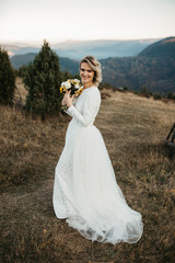 Fototapeta na wymiar Portrait of Beautiful elegant bride in lace wedding dress with long full skirt and long sleeves. Pretty girl in white. Nature, with city in the background, sunset time.