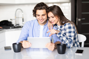 Young couple eating breakfast using digital tablet in modern kitchen