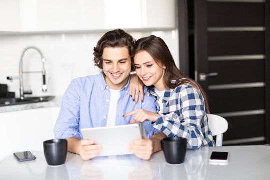 Young couple eating breakfast using digital tablet in modern kitchen