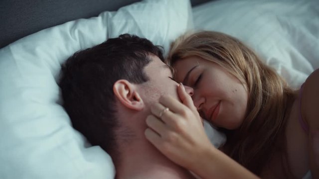 Couple in bed gently stroking each other . white sheets, delicate tones