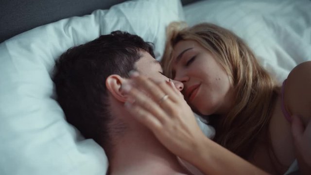 Couple in bed gently stroking each other . white sheets, delicate tones