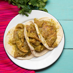 Mexican pork chicharron with green sauce tacos on turquoise background