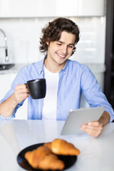 Portrait of happy man eat at breakfast and using digital tablet in kitchen at home
