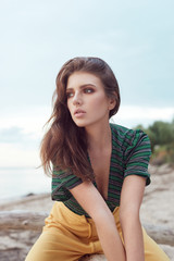 Portrait of a beautiful young girl on the beach wearing a green blouse and yellow pants, stylish retro clothing, lifestyle and fashion