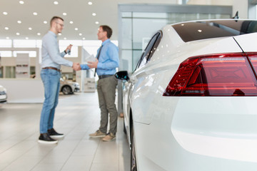  Shaking hands after a successful car buying in modern car showroom. Focus on the vehicle