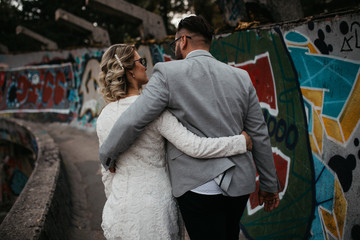 Beautiful couple having a romantic moment on their weeding day, in mountains at sunset. Bride is in a white wedding dress with a bouquet of sunflowers in hand, groom in a suit. Happy hugging couple.