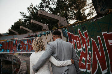 Beautiful couple having a romantic moment on their weeding day, in mountains at sunset. Bride is in a white wedding dress with a bouquet of sunflowers in hand, groom in a suit. Happy hugging couple.