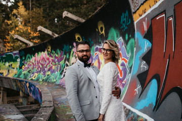 Beautiful couple having a romantic moment on their weeding day, in mountains at sunset. Bride is in a white wedding dress with a bouquet of sunflowers in hand, groom in a suit. Happy hugging couple.