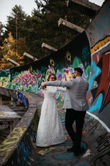 Beautiful couple having a romantic moment on their weeding day, in mountains at sunset. Bride is in a white wedding dress with a bouquet of sunflowers in hand, groom in a suit. Happy hugging couple.