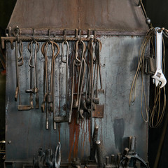 blacksmith and locksmith tools are hung on the metal wall of the forge furnace