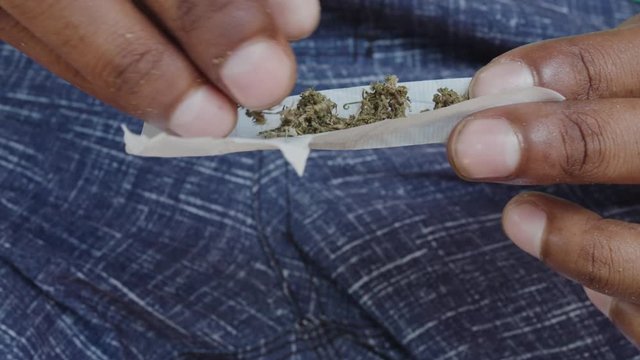 beautiful cinematic footage of a man male rolling weed marihuana cigaret joint while sitting on a bench