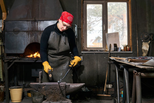 female blacksmith metal artist forges a figured metal blank on the anvil