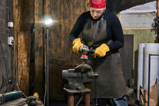 female artisan processes a metal artwork with an angle grinder - Powered by Adobe