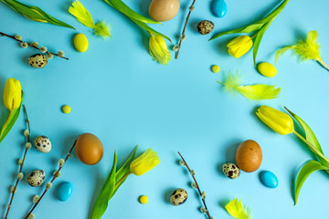 Fototapeta premium Happy Easter frame with yellow tulips, easter eggs, quail eggs, pussy-willow twigs, colored sweet balls with place for text in the middle. Easter background top view,copy space