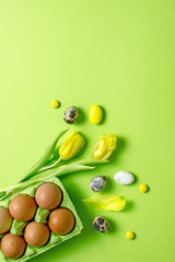 Easter greeting card with yellow eggs, yellow tulips, quail eggs, sweet colored balls on a green background, top view, copy space, Vertical background
