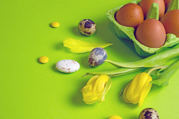 Fototapeta na wymiar Easter greeting card with yellow eggs, yellow tulips, quail eggs, sweet colored balls on a green background, top view, copy space.