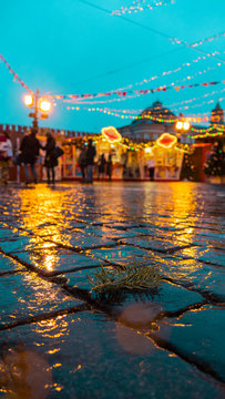 Tree branch on wet paving stones with BOKEH.Against the background of bright lights (garlands) of the fair, the walls of the Kremlin and people.