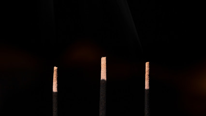 Indian incense sticks. Burning, brown incense sticks on a dark background. Smoke with aroma rises. Ashes after smoldering. Closeup. The concept of Indian culture, Buddhism and religion.