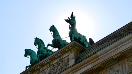 Fototapeta na wymiar Brandenburg Gate against the sun. Close up. Major landmark and national symbol of Berlin, Germany. Statue of the Goddess Victoria with Horses on Brandenburg Tor. Viewed from the Pariser Platz. 