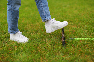 Woman in white sneakers and jeans stepping accidentally on a rake on green grass. Carelessness concept, same mistake, lifestyle. Working outdoor in garden, safety, instrument. Close up, copy space