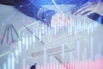 Double exposure of man's hands writing notes of stock market with forex chart.