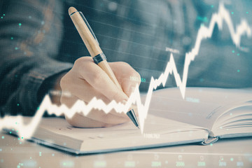 Double exposure of woman's hands making notes with forex graph hologram. Concept technical analysis.