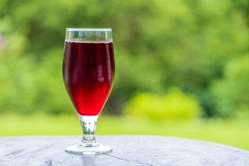 Glass with tropical red juice from leaf hibiscus on the wooden table in yard, close up, Tanzania, Africa, copy space