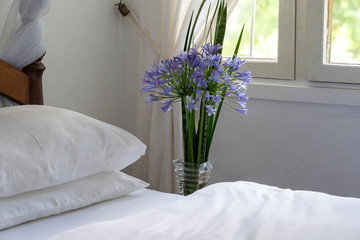 Comfortable soft bed in room and a bouquet of flowers near the window, close up