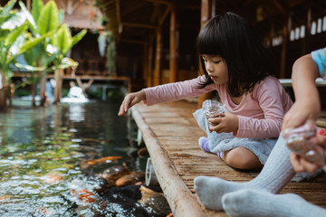 two little girls having fun feeding koi fish by the pond
