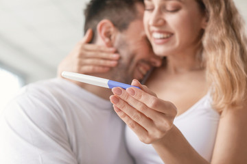 Happy young couple with pregnancy test in bathroom, closeup