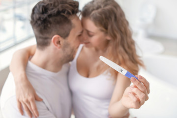 Happy young couple with pregnancy test in bathroom