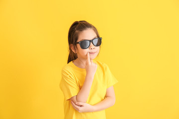 Funny little girl with sunglasses on color background