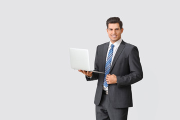 Handsome businessman with laptop on light background