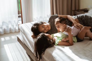 two little daughter lying in bed with their mother next to them in the bedroom