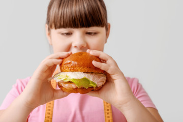 Overweight girl with unhealthy burger on light background