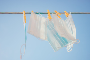 Medical face masks hanging on a clothesline with yellow clothespins in blue sky background.