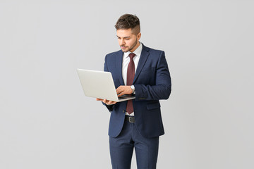 Handsome businessman with laptop on light background